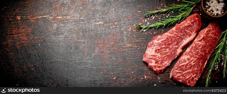 Raw steak with rosemary and spices on the table. Against a dark background. High quality photo. Raw steak with rosemary and spices on the table.