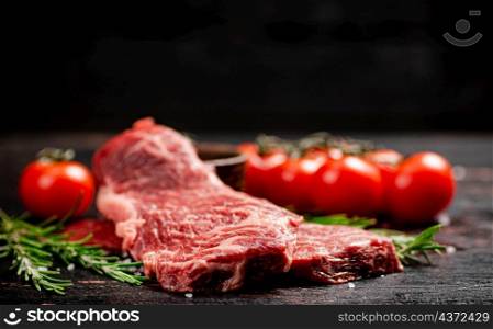 Raw steak with rosemary and spices on the table. Against a dark background. High quality photo. Raw steak with rosemary and spices on the table.
