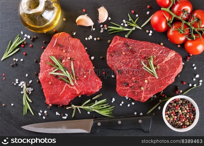 Raw steak with rosemary, salt and pepper on black slate background. ingredients for cooking beefsteak, tomato, olive oil, rosemary, spices.. Fresh raw beef steak with spice on black background