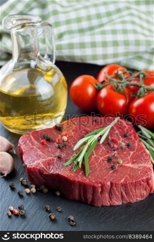 Raw steak with rosemary, salt and pepper on black slate background. ingredients for cooking beefsteak, tomato, olive oil, rosemary, spices. Vertical orientation. Fresh raw beef steak with spice on black background