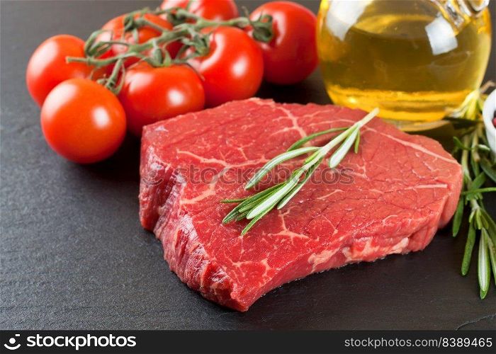 Raw steak with rosemary, salt and pepper on black slate background. ingredients for cooking beefsteak, tomato, olive oil, rosemary, spices.. Fresh raw beef steak with spice on black background