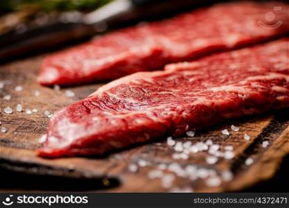 Raw steak with spices on a wooden cutting board. Macro background. High quality photo. Raw steak with spices on a wooden cutting board.