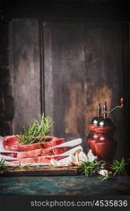 Raw steaks with herbs,spices and salt and pepper mills on kitchen table at dark rustic background, side view, place for text, dinner preparation