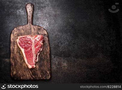 Raw T-bone steak on aged wooden cutting board on dark rust metal background, top view, place for text