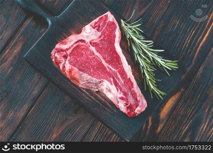 Raw T-bone steak with fresh rosemary and red peppercorn