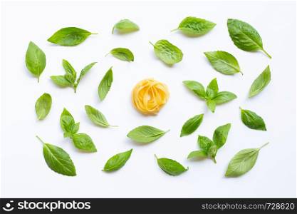 Raw tagliatelle pasta with basil leaves on white background.