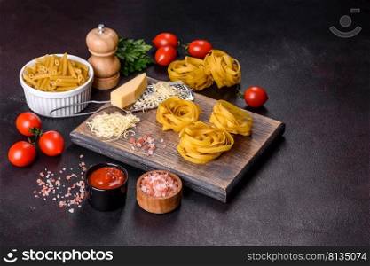 Raw tagliatelle paste with grated cheese, cherry tomatoes, spices and herbs on a wooden cutting board against a dark concrete background. Raw tagliatelle paste with grated cheese, cherry tomatoes, spices and herbs on a wooden cutting board