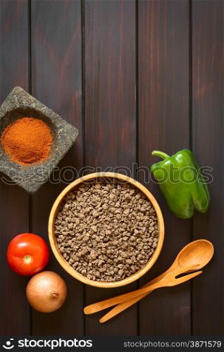 Raw textured vegetable or soy protein, called also soy meat in wooden bowl with raw vegetables and paprika in mortar. Photographed overhead on dark wood with natural light.