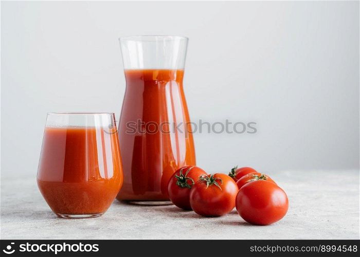 Raw tomatoes and glass of freshly drink, isolated over white background. Tomato juice made of vegetables in transparent glasses. Healthy drink
