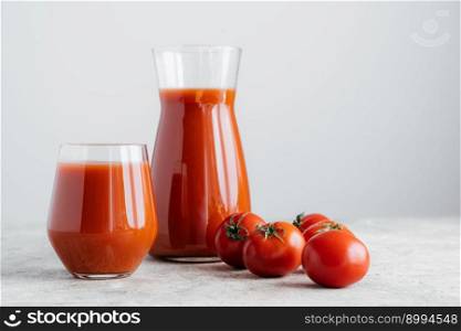Raw tomatoes and glass of freshly drink, isolated over white background. Tomato juice made of vegetables in transparent glasses. Healthy drink