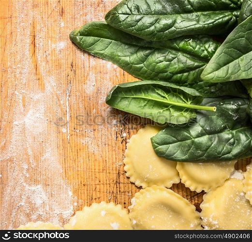 Raw Tortellini with fresh spinach leaves on wooden background with wheat flour, top view, place for text