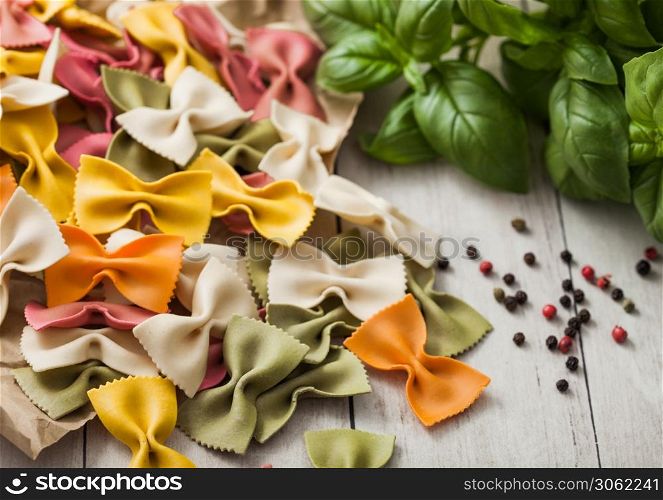 Raw tricolore farfalle pasta in brown paper on light wooden table background with basil and garlic. Macro