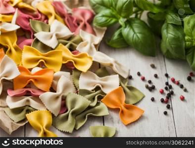 Raw tricolore farfalle pasta in brown paper on light wooden table background with basil and garlic. Macro