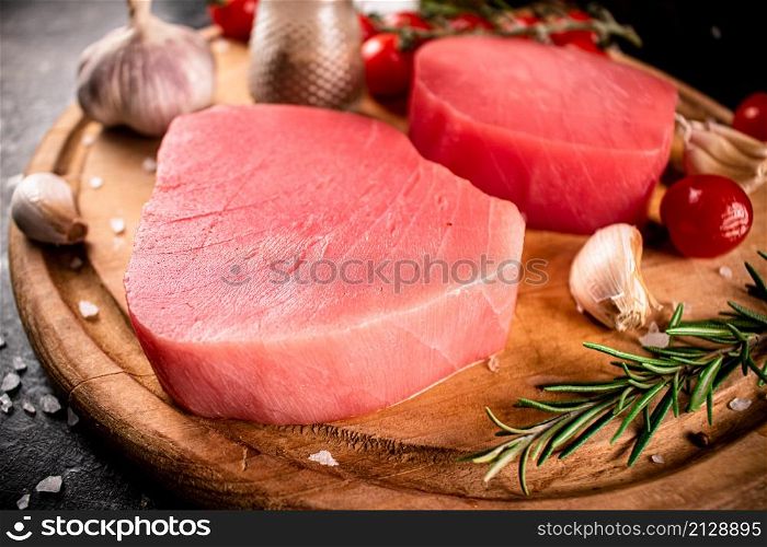 Raw tuna on a cutting board with garlic, tomatoes and spices. On a black background. High quality photo. Raw tuna on a cutting board with garlic, tomatoes and spices.