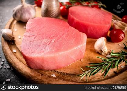 Raw tuna on a cutting board with garlic, tomatoes and spices. On a black background. High quality photo. Raw tuna on a cutting board with garlic, tomatoes and spices.