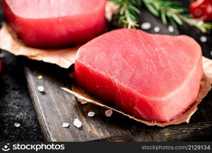 Raw tuna on a cutting board with tomatoes and rosemary. On a black background. High quality photo. Raw tuna on a cutting board with tomatoes and rosemary.