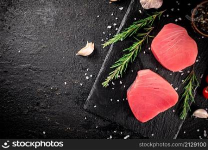 Raw tuna on a stone board with rosemary and garlic. On a black background. High quality photo. Raw tuna on a stone board with rosemary and garlic.
