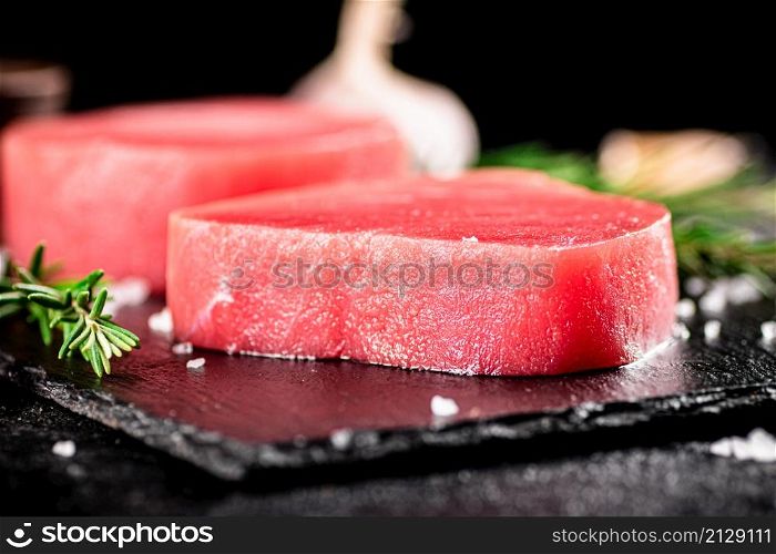 Raw tuna on a stone board with rosemary and garlic. On a black background. High quality photo. Raw tuna on a stone board with rosemary and garlic.