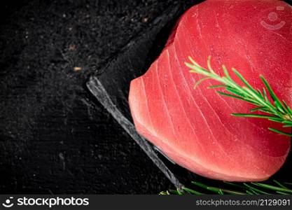 Raw tuna on a stone board with rosemary. On a black background. High quality photo. Raw tuna on a stone board with rosemary.