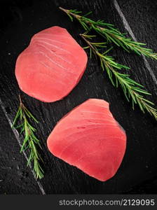 Raw tuna on a stone board with rosemary. On a black background. High quality photo. Raw tuna on a stone board with rosemary.