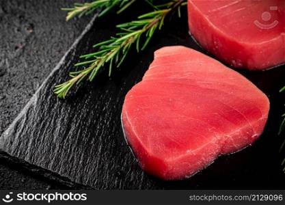 Raw tuna on a stone board with rosemary. On a black background. High quality photo. Raw tuna on a stone board with rosemary.