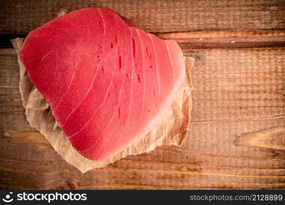 Raw tuna steak with paper on the table. On a wooden background. High quality photo. Raw tuna steak with paper on the table.