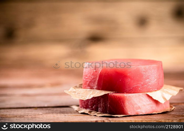 Raw tuna steak with paper on the table. On a wooden background. High quality photo. Raw tuna steak with paper on the table.