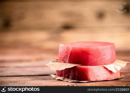 Raw tuna steak with paper on the table. On a wooden background. High quality photo. Raw tuna steak with paper on the table.