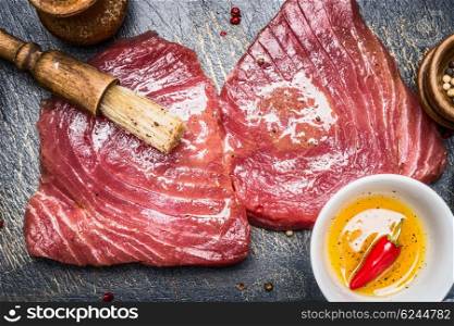 Raw tuna steaks marinating for grill or cooking with brush and spices oil, top view, close up