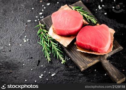 Raw tuna steaks on a rosemary cutting board. On a black background. High quality photo. Raw tuna steaks on a rosemary cutting board.