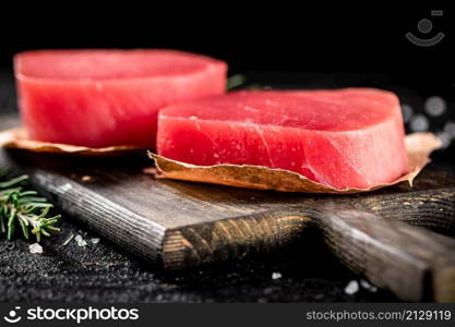 Raw tuna steaks on a rosemary cutting board. On a black background. High quality photo. Raw tuna steaks on a rosemary cutting board.