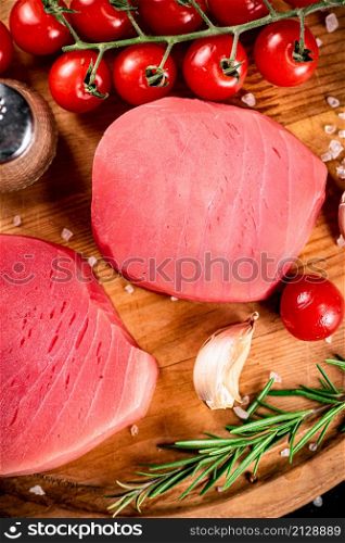 Raw tuna with cherry tomatoes and rosemary. On a wooden background. High quality photo. Raw tuna with cherry tomatoes and rosemary.