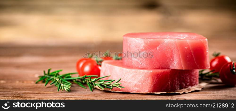 Raw tuna with cherry tomatoes and rosemary. On a wooden background. High quality photo. Raw tuna with cherry tomatoes and rosemary.