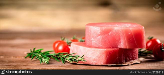 Raw tuna with cherry tomatoes and rosemary. On a wooden background. High quality photo. Raw tuna with cherry tomatoes and rosemary.