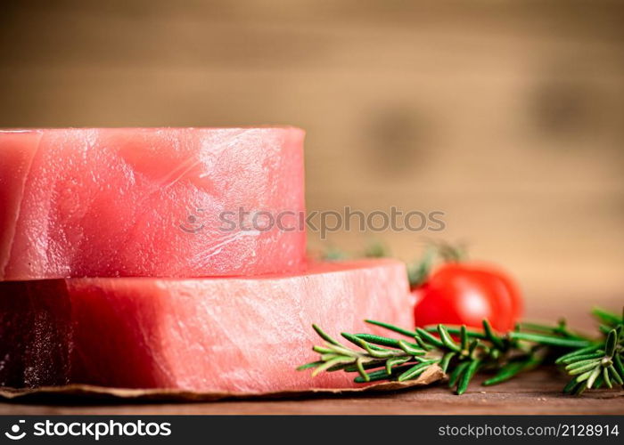 Raw tuna with cherry tomatoes and rosemary. On a wooden background. High quality photo. Raw tuna with cherry tomatoes and rosemary.