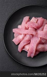 Raw turkey meat in the form of slices with salt, spices and herbs on a dark concrete background