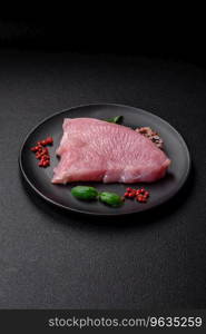 Raw turkey meat in the form of slices with salt, spices and herbs on a dark concrete background