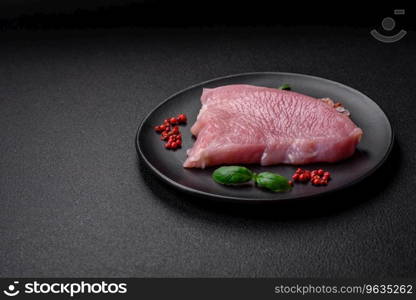 Raw turkey meat in the form of slices with salt, spices and herbs on a dark concrete background