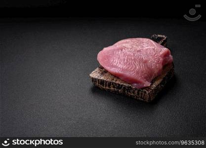 Raw turkey meat in the form of slices with salt, spices and herbs on a dark concrete background