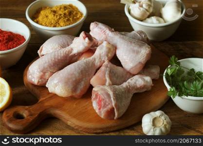 Raw uncooked chicken legs, drumsticks on cuttingn board, meat with ingredients for cooking. Raw uncooked chicken legs, drumsticks on cutting board, meat with ingredients for cooking