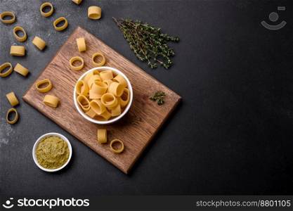 Raw uncooked pasta in a white ceramic bowl with spices and herbs on a dark concrete background