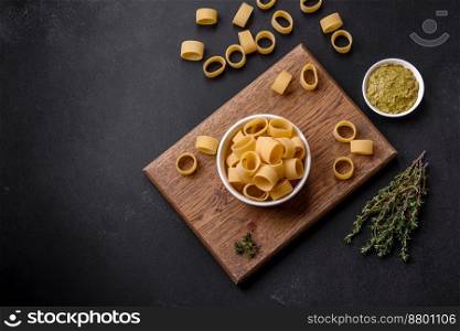 Raw uncooked pasta in a white ceramic bowl with spices and herbs on a dark concrete background