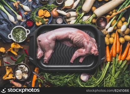 Raw uncooked whole rabbit and various cooking ingredients for stew or ragout. Rabbit stew preparation with forest mushrooms and vegetables of autumn season on dark rustic background, top view