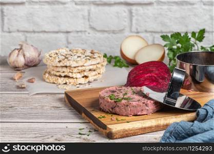 Raw veggie burger with beetroot and white beans with parsley leaves on wood cutting board