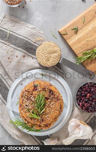 Raw veggie burger with quinoa, red beens, vegetables and rosemary leaves on kitchen countertop