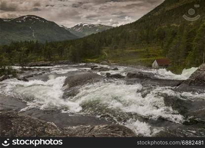 raw waterfall with small house and mountains with snow as background near Balestrand