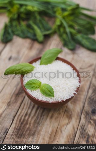 raw white rice bowl with fresh basil leaves weathered wooden plank