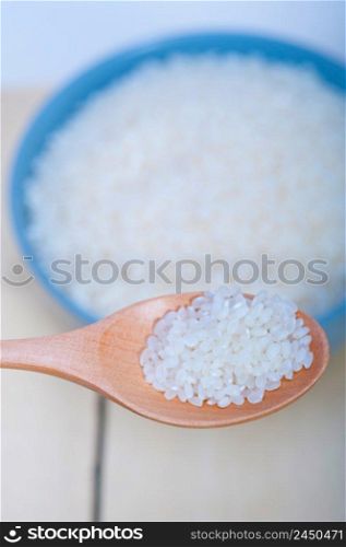 raw white rice on wood spoon and blue bowl extreme close up 