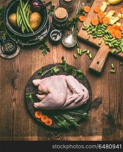 Raw whole chicken on rustic wooden kitchen table background with vegetables, cooking spoon and cutting board, top view. Chicken cooking preparation