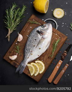 Raw whole dorado fish on wooden kitchen board and spices for cooking, top view on black table